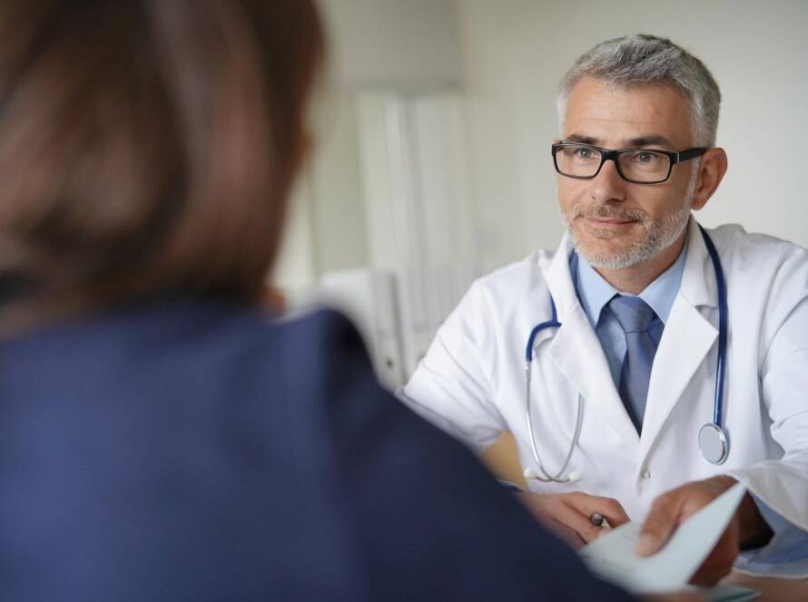 Arzt im Gespräch mit einer Patientin, überreicht eine Überweisung
