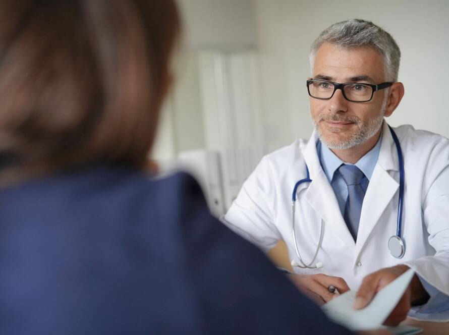 Arzt im Gespräch mit einer Patientin, überreicht eine Überweisung